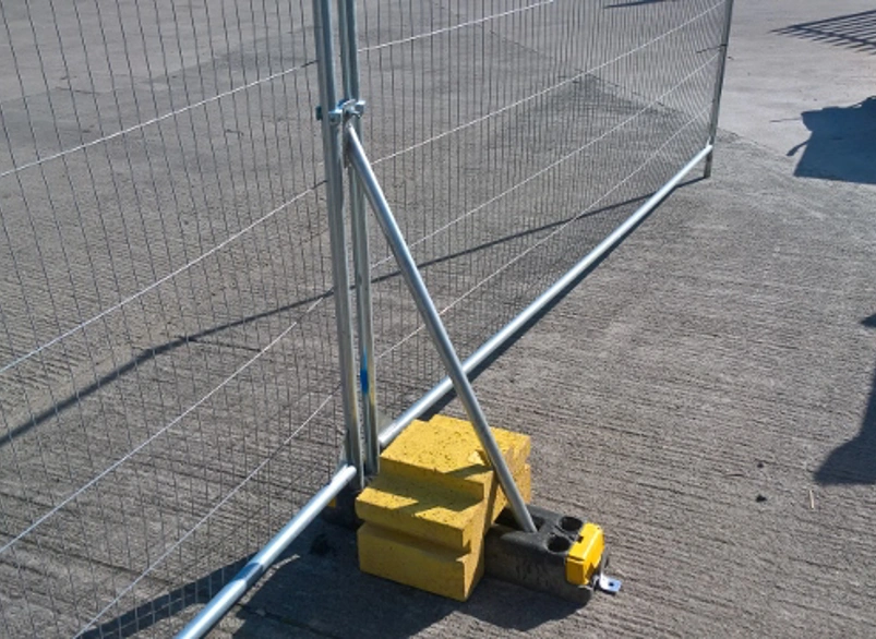 Temporary mesh construction fence panel secured with bracing and ballast blocks on pavement