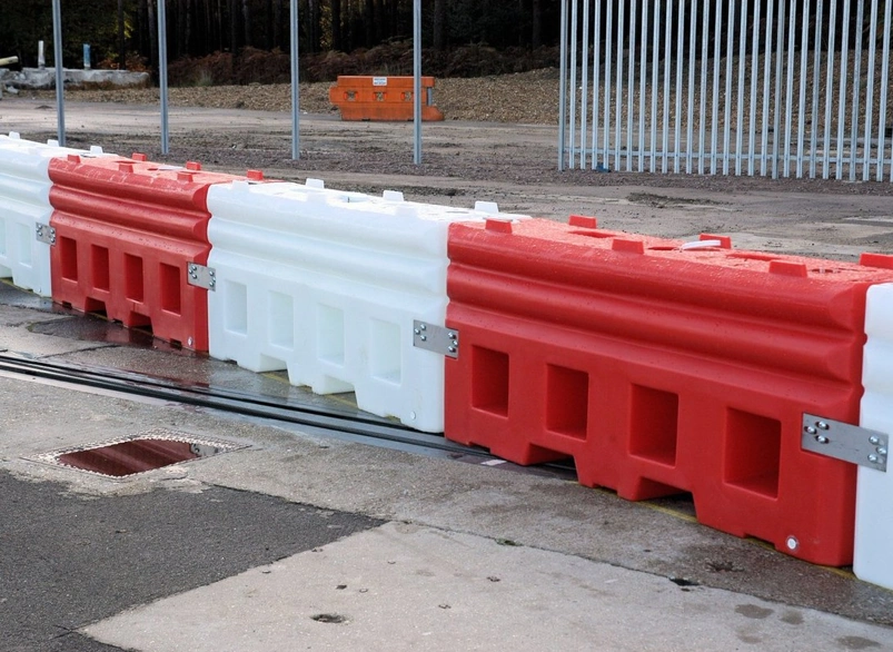 Interlocking red and white water-filled traffic barriers protecting a roadside work area