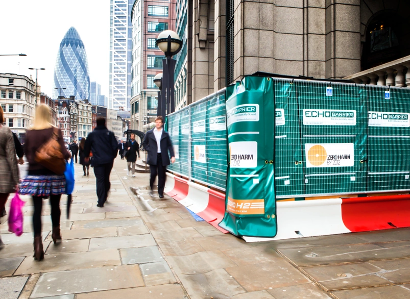 Green construction hoarding and safety echo barriers on a busy London street near the Gherkin