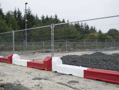 Temporary mesh security fencing with red and white water-filled slot barriers at a construction site