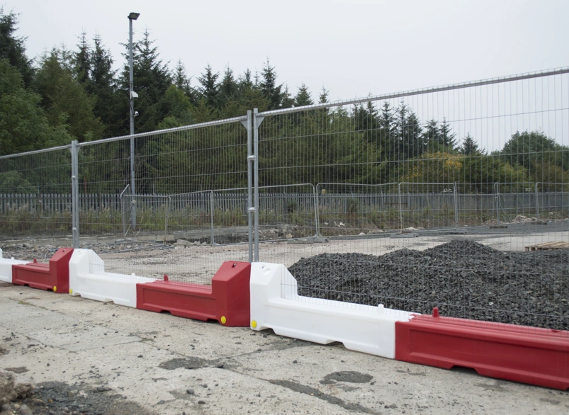 Temporary mesh security fencing with red and white water-filled slot barriers at a construction site