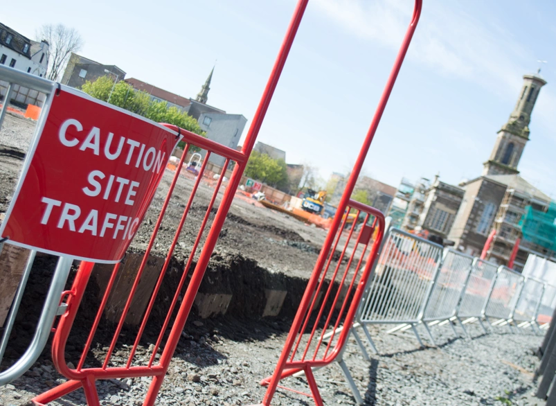 Red safety crowd barrier entry with caution site traffic sign at an urban construction site